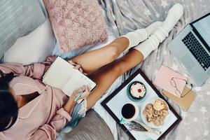 Top view of beautiful young woman in pajamas writing something down while resting in bed at home photo