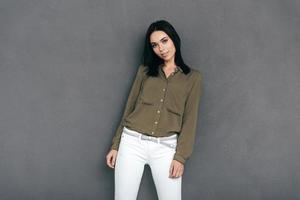 Confident in her perfect style. Attractive young woman in smart casual wear standing against grey background and looking at camera photo