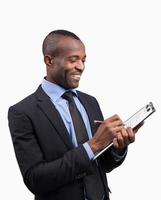 Making notes. Cheerful young African man in formalwear making notes in his note pad and smiling while standing against grey background photo