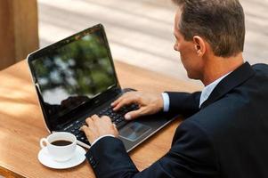 trabajando al aire libre. vista superior del hombre maduro en ropa formal trabajando en la computadora portátil mientras está sentado en la mesa al aire libre foto