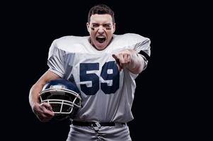 Unleashed emotions.  American football player screaming and pointing at camera while standing against black background photo