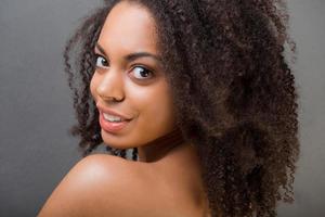 Feeling flirty. Attractive young shirtless African woman looking over shoulder and smiling while standing against grey background photo