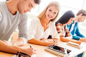 I love studying Smiling young woman looking at camera and smiling while her classmates writing something photo