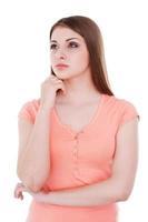 Lost in thoughts. Thoughtful young woman holding hand on chin and looking away while standing isolated on white photo