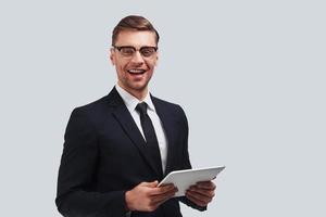 How may I help you Handsome young man using digital tablet and smiling while standing against grey background photo