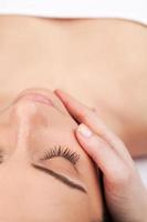 Facial massage. Top view of attractive young woman lying down and keeping eyes closed while massage therapist massaging her face photo