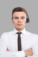 Customer service representative. Cheerful young man in formalwear adjusting his headset and smiling at camera while standing against grey background photo