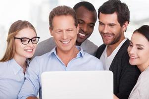 Creative team at work. Group of business people in casual wear standing close to each other and looking at the laptop photo