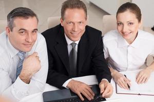 Business people at work. Top view of three cheerful business people in formalwear sitting at the table and looking at camera photo