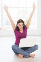 I did it Happy young woman keeping arms raised and expressing positivity while working at laptop in her apartment photo