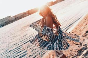 Feeling free to express her sensuality.  Attractive young woman smiling while standing on the beach outdoors photo