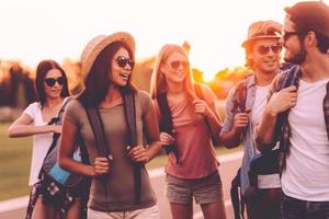 In search of adventures. Group of young people with backpacks walking together by the road and looking happy photo