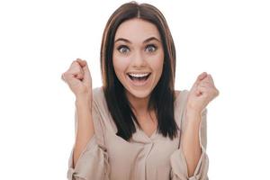 Feeling so happy now. Beautiful young woman gesturing and looking happy while standing against white background photo