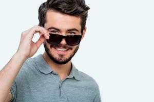 sonrisa confiable. alegre joven ajustando gafas y sonriendo a la cámara mientras está de pie contra el fondo blanco foto