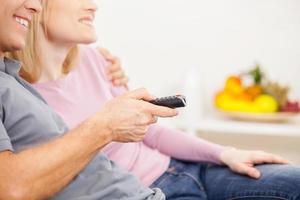 Switching TV channels. Side view cropped image of cheerful mature couple sitting together and watching TV photo