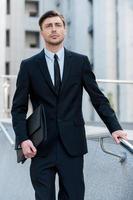 Young and successful. Full length of cheerful young men in formalwear holding briefcase while walking outdoors photo