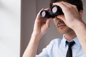 Looking for new opportunities. Confident young man in shirt and tie looking through binoculars photo