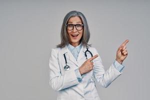 Mature beautiful female doctor looking at camera and pointing copy space photo