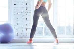 Close-up rear view of young sporty woman with perfect buttocks standing in front of window at gym photo