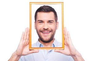 retrato de mí apuesto joven en camisa mirando a la cámara a través del marco de la imagen mientras está de pie contra el fondo blanco foto