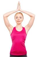 Yoga as a lifestyle. Beautiful mature women holding hands over head and looking at camera while standing against white background photo