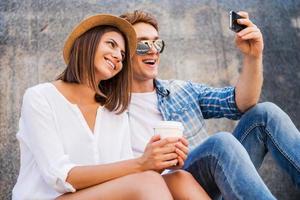 Capturing the bright moments. Happy young loving couple making selfie with smart phone while leaning at the wall photo