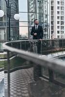 Feeling happy. Good looking young man in full suit looking away and smiling while standing outdoors photo