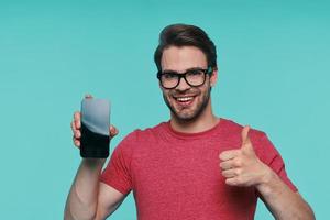 Portrait of handsome young smiling man in eyeglasses showing his smart phone and gesturing photo