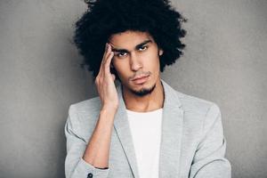 Did you ever have such headache Frustrated young handsome African man looking exhausted and looking at camera while standing against grey background photo