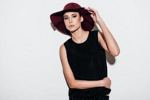 Real lady. Beautiful young woman adjusting her hat and looking at camera while standing against white background photo