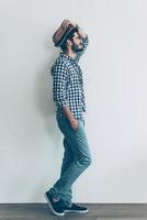 Feeling casual. Full length side view of handsome young cheerful man holding one hand in pocket and adjusting his hat photo