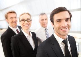 equipo exitoso joven alegre con ropa formal mirando a la cámara y sonriendo mientras sus colegas están detrás de él foto