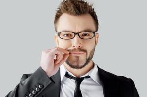 I will say nothing. Portrait of young man in formalwear closing his mouth by hand while standing against grey background photo