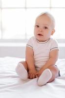 Pretty baby. Little baby sitting on the bed and looking at camera photo