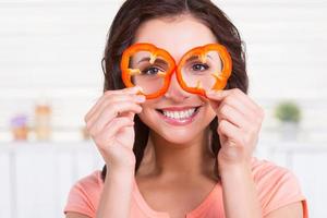 Kitchen fun. Portrait of playful young woman looking through the pieces of red pepper and smiling while standing in the kitchen photo