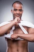 Taking his shirt away. Handsome young African man taking off his tank top and smiling while standing against grey background photo