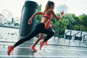 Full length of motivated young man and woman in sports clothing jumping and jogging while exercising on the city street outdoors photo