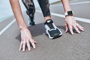 dando todo lo mejor de ella. Cerca de una joven con ropa deportiva parada en la línea de salida mientras corre al aire libre foto