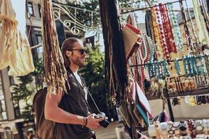 Souvenirs. Handsome young man in casual clothing standing near the market stall while spending time outdoors photo