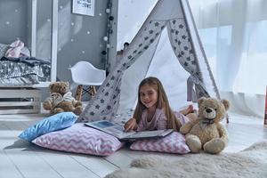 Time for great stories. Cute little girl pointing in book while lying on the floor in tent photo