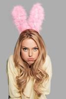 Bored bunny. Attractive young woman in pink bunny ears making a face and looking at camera while standing against grey background photo