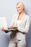 In love with her work. Confident young businesswoman holding laptop while standing against grey background photo