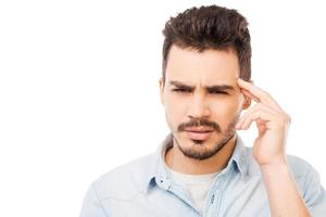 Feeling headache. Frustrated young man in shirt touching head and looking at camera while standing against white background photo