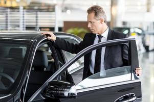 Examining his new car. Confident mature man in formalwear opening the car door at the dealership photo