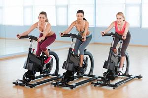 ciclismo en bicicletas estáticas. dos mujeres jóvenes atractivas en ropa deportiva haciendo ejercicio en bicicletas de gimnasio foto