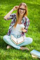 Happy student. Top view of beautiful young female student adjusting her glasses and smiling while sitting in a park with books around her photo