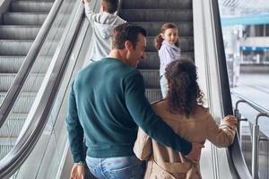 Happy family with two little kids moving by escalator in airport terminal photo