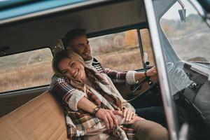 ella significa todo para él. hermosa pareja joven abrazándose y sonriendo mientras se sienta en una mini furgoneta de estilo retro foto