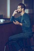 I am waiting for you Side view of handsome young man talking on mobile phone with smile while sitting at bar counter photo