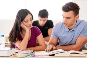 tenemos que aprender este capítulo. dos estudiantes confiados leyendo un libro juntos mientras están sentados en el aula foto